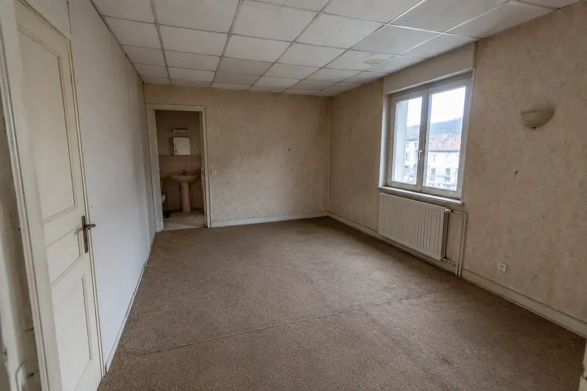 Pièce d’un appartement ancien avant curage, avec faux plafond, moquette et papier peint